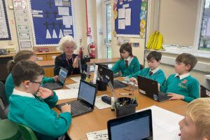 An elderly member of the Horsmonden Nostalgia Society is pictured sharing her perspectives on the war with some Horsmonden students sat around a table.