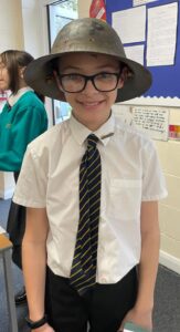 A young boy is pictured smiling for the camera whilst wearing a WWII soldier's helmet on his head.