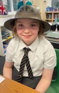 A young girl is pictured smiling for the camera whilst wearing a WWII soldier's helmet on her head.
