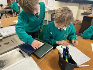 Two boys in academy uniform are pictured sat together at a desk and looking at some memorabilia from WWII.