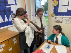 Three girls are seen dressed in academy uniform, interacting with some memorabilia from WWII.