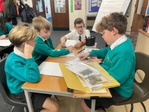 Four boys are pictured sat together at a desk, looking at some memorabilia from WWII.