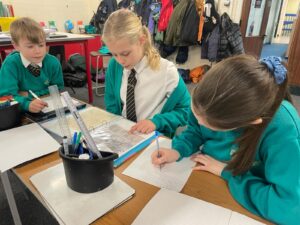 Three young pupils in academy uniform can be seen sat around a table, examining some documents from WWII.