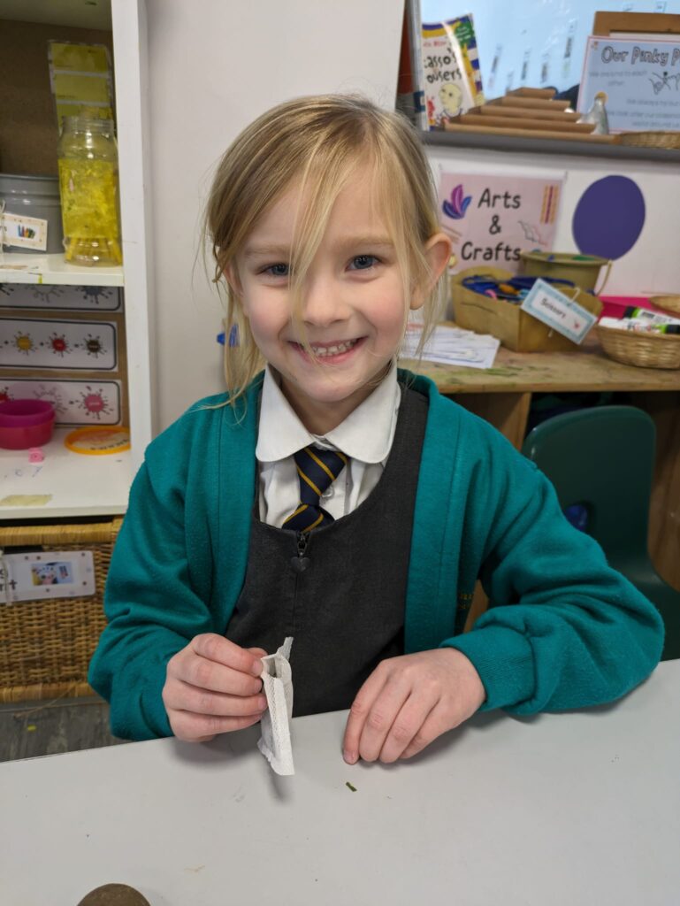 A female student is pictured smiling for the camera, whilst holding a teabag in her hand.