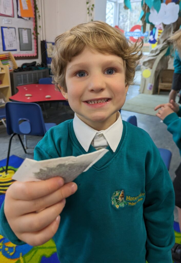 A male student is pictured smiling for the camera, whilst holding a teabag in his hand.
