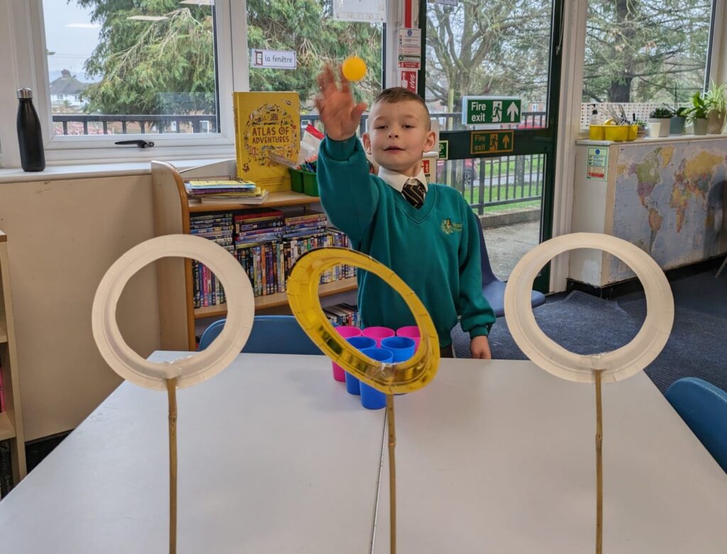 A male student is seen smiling, as he practices throwing balls through large hoops on sticks he has created.