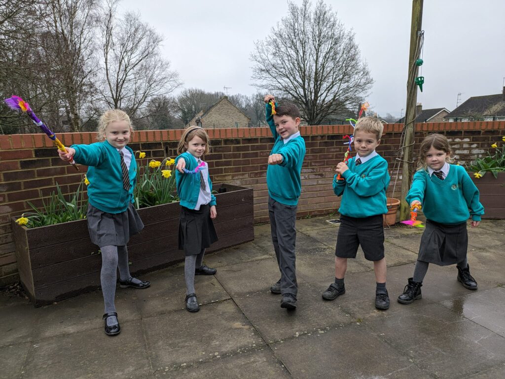 Five young students are pictured posing for the camera with the wands they have made from craft materials.