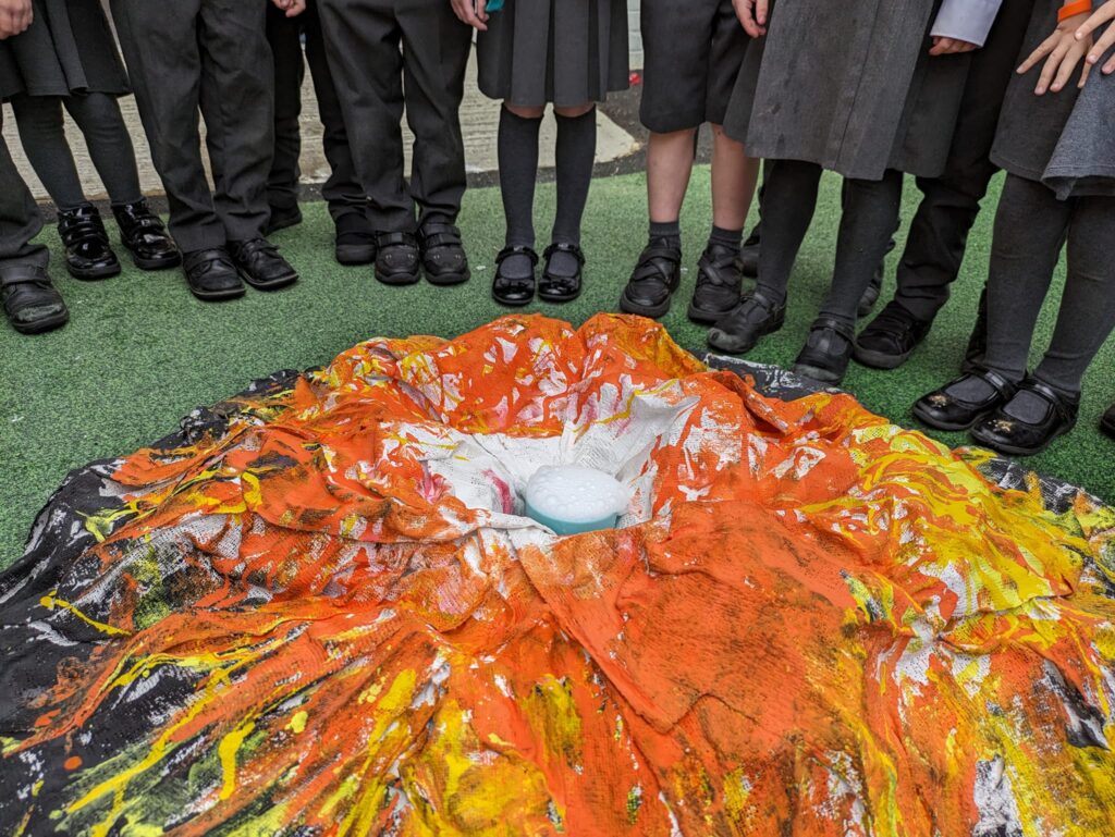 A group of EYFS pupils are pictured stood around a model of an erupting volcano that they have made together.