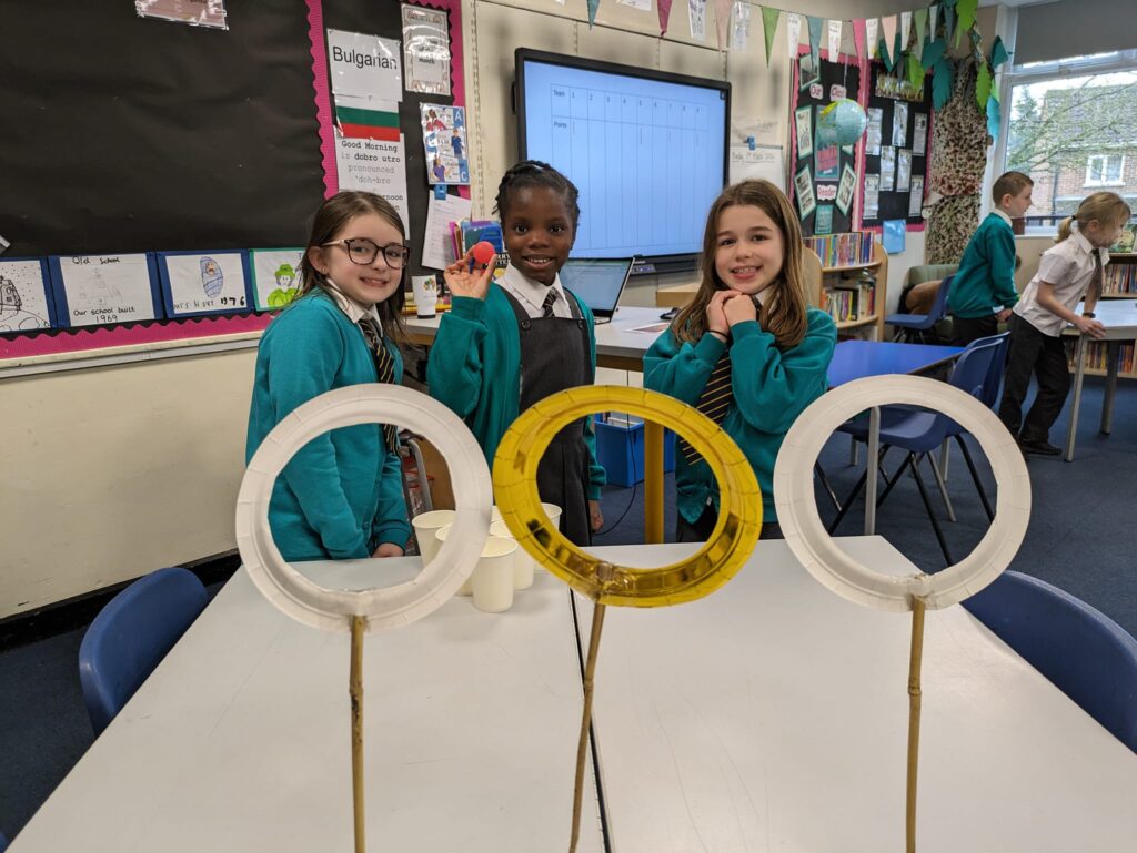3 students throwing balls through small hoops on the table