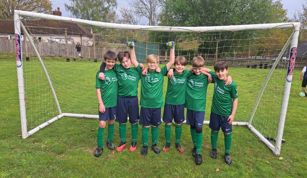 Six male pupils from Year 5 are pictured smiling together for the camera in front of a goalpost, after having just won a Football match.