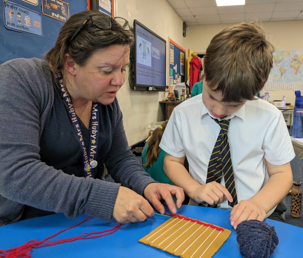 A male pupil from Year 3 is pictured creating his own loom, with the assistance of a member of staff, during a Design & Technology class.