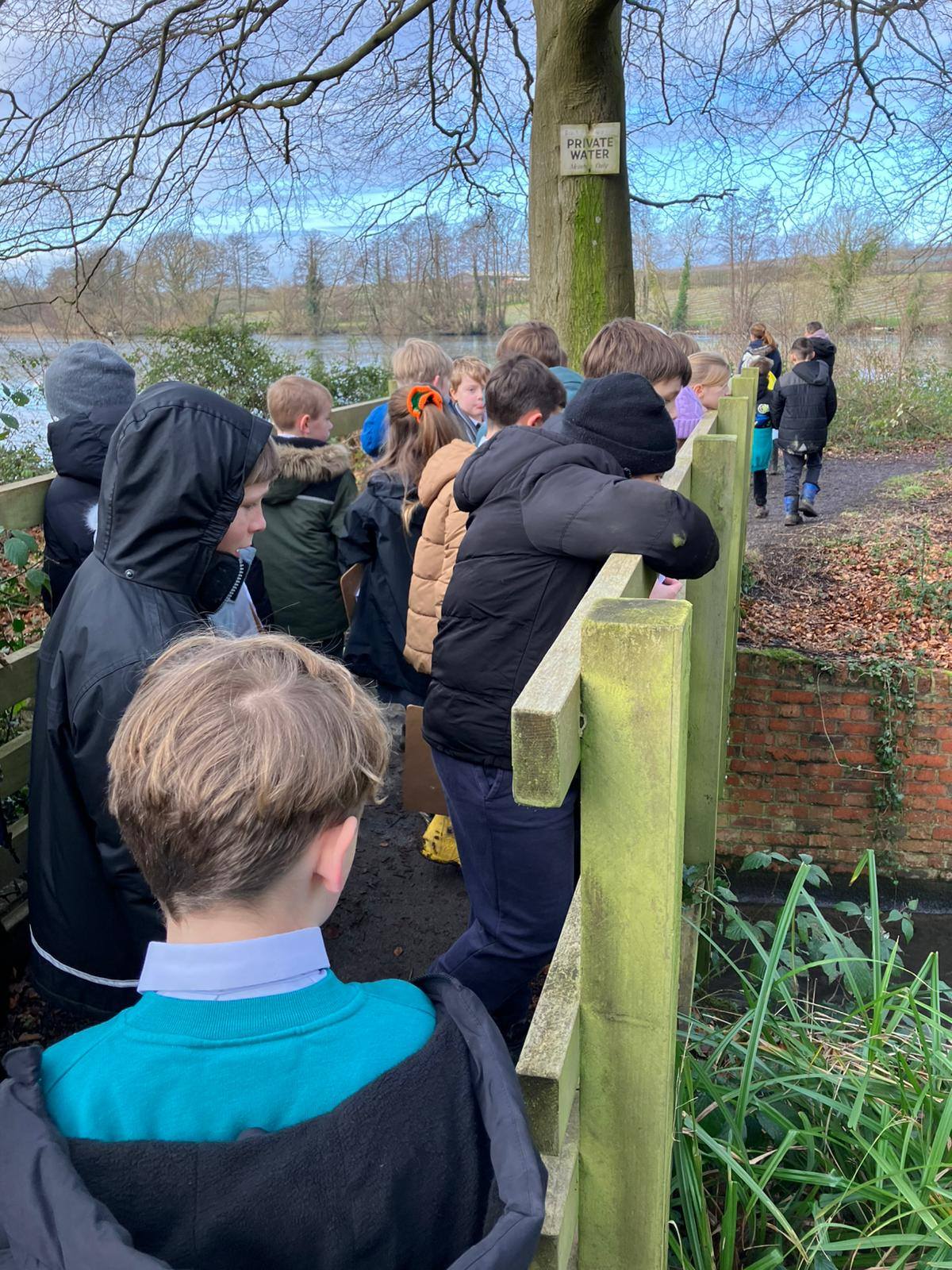 A group of students looking over a wooden bridge railing at a stream