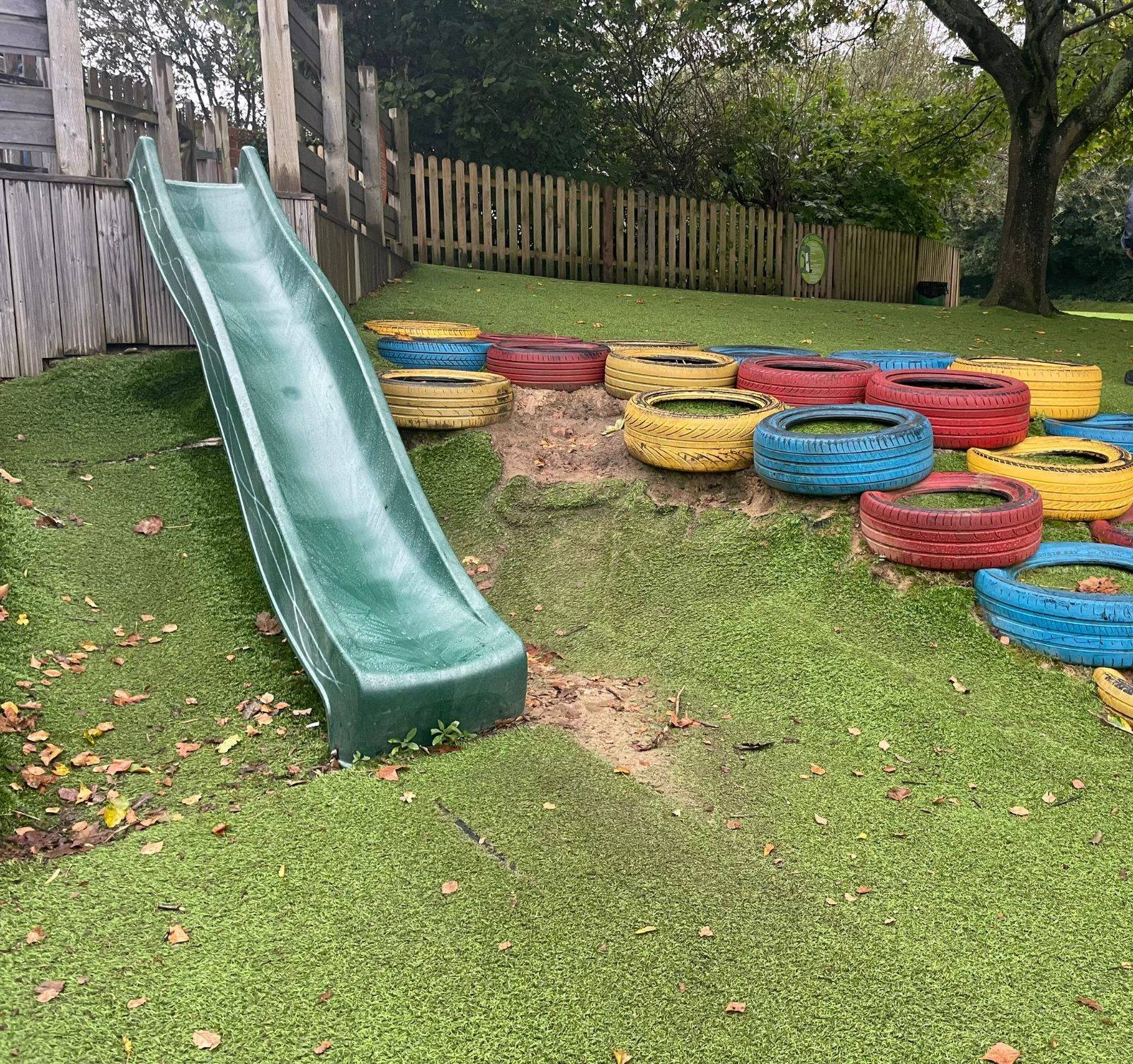 A slide in a playground next to painted tyres