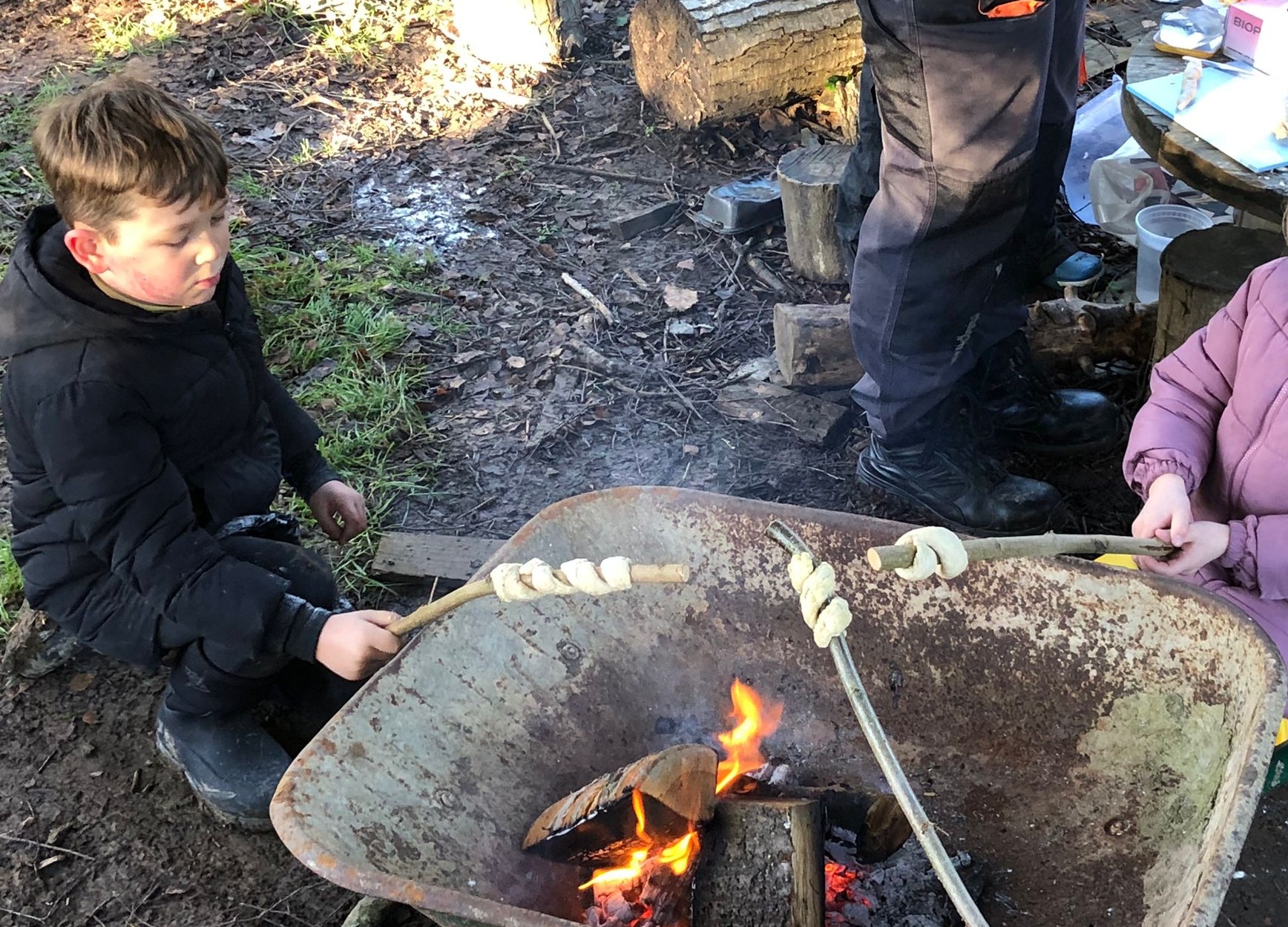 Students roasting marshmallows over a wheelbarrow containing a small fire
