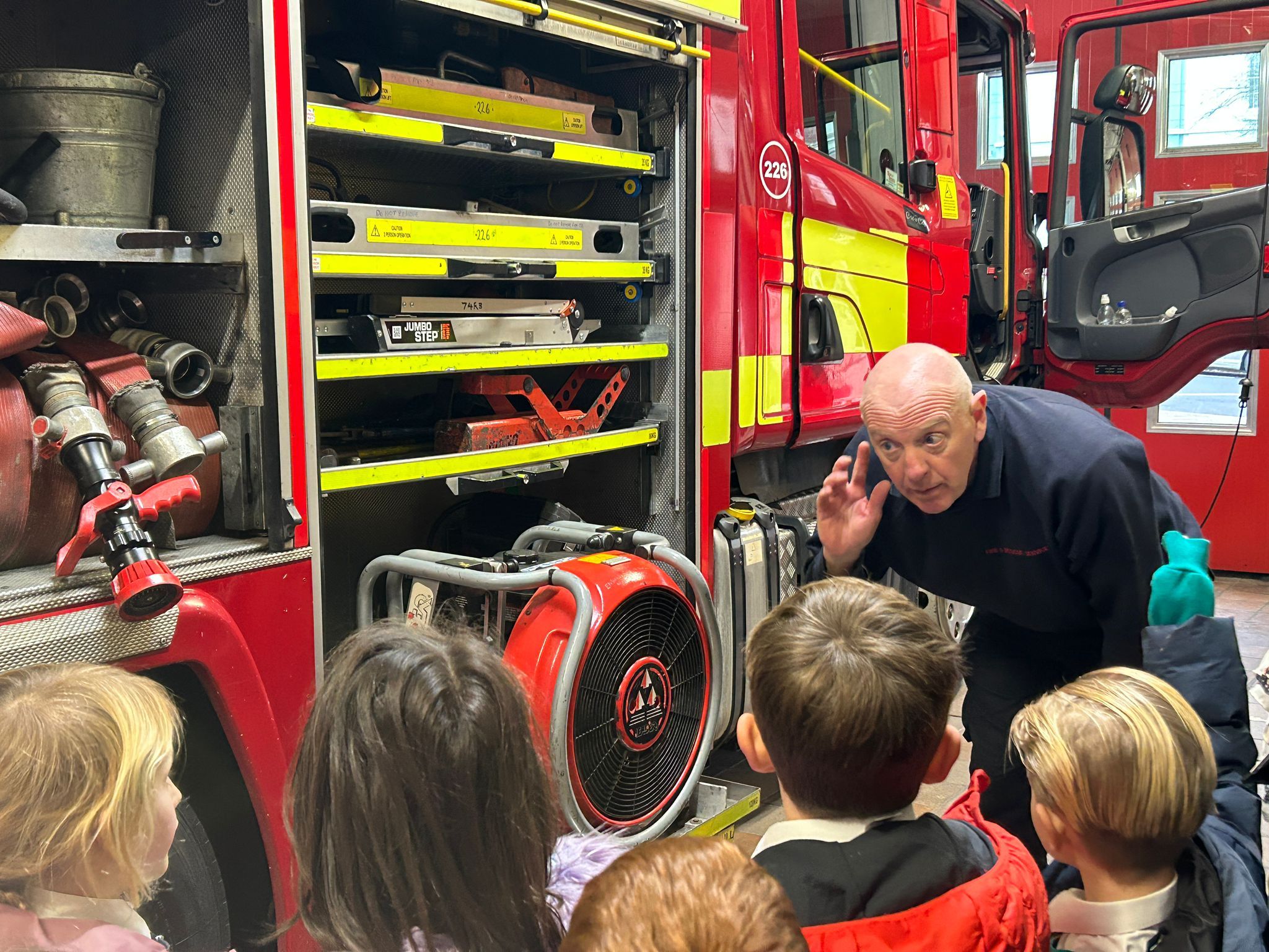 A group of students listening to a firefighter talking in front of a fire engine