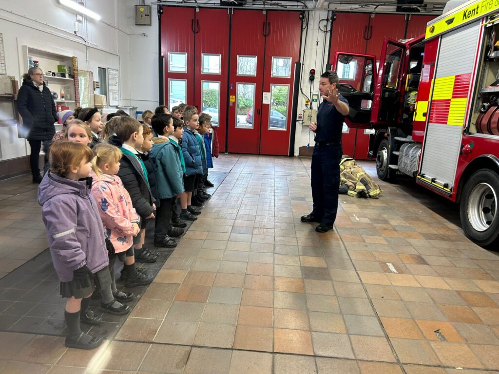 A group of students listening to a firefighter talking in front of a fire engine