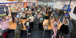 Students in a classroom holding up their artwork and smiling