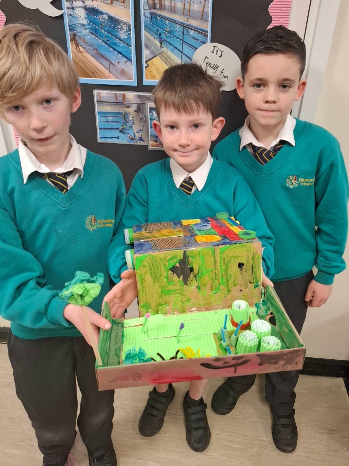 3 students smiling, holding up their project