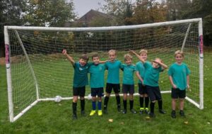 Seven boys pose for a picture in a football goal in their PE kits of green t-shirts and black shorts