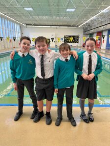 4 pupils in school uniform pose for a picture in front of an indoor swimming pool